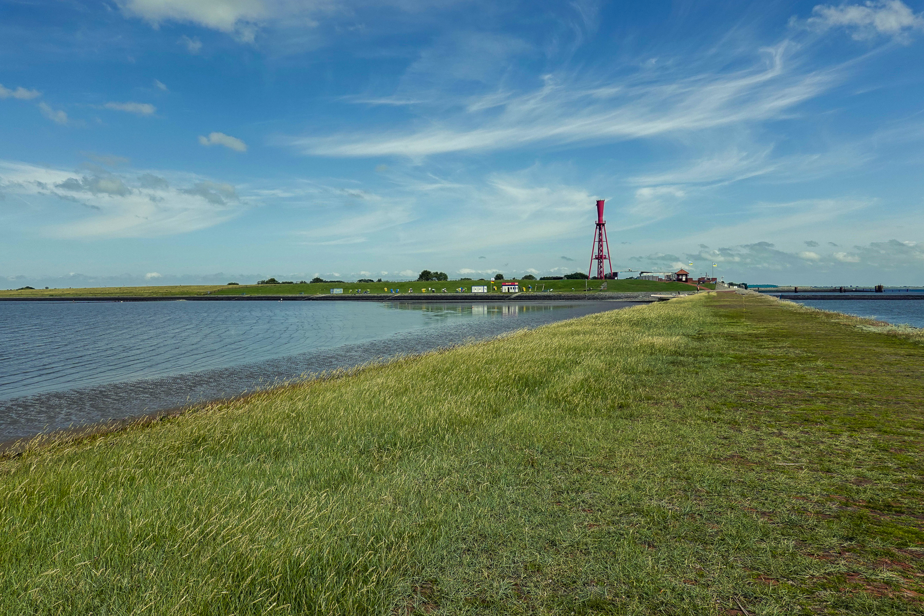 Küstenweg bei Butjadingen mit Meer und Grasflächen, tiefem Horizont und wolkigem Himmel, fotografiert an der Nordsee im Sommer